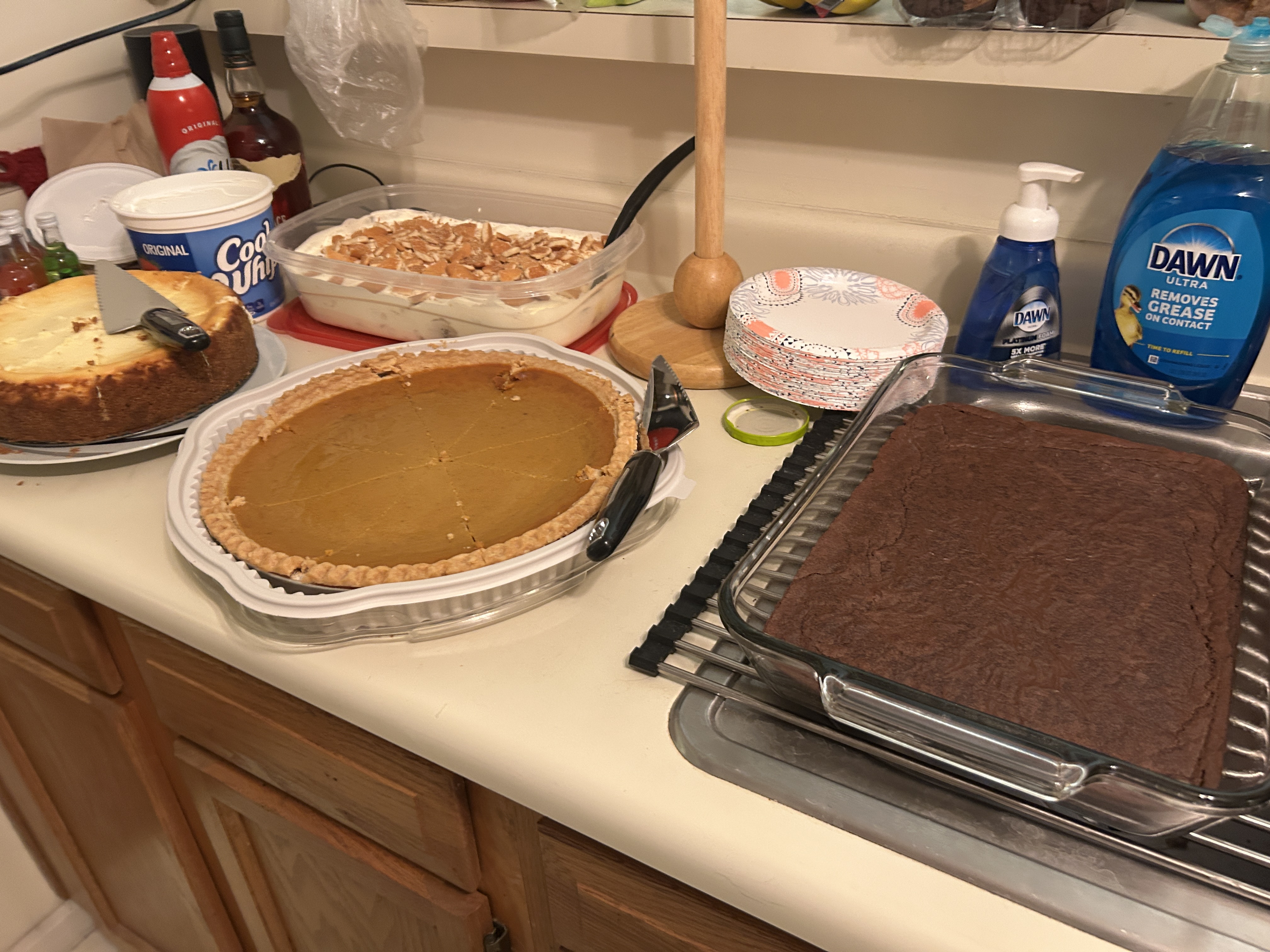 Banana pudding, brownies, cheesecake, and pumpkin pie on a counter.